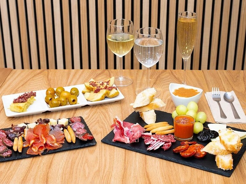 A tapas board of cured meats, cheese and olives with glasses of wine